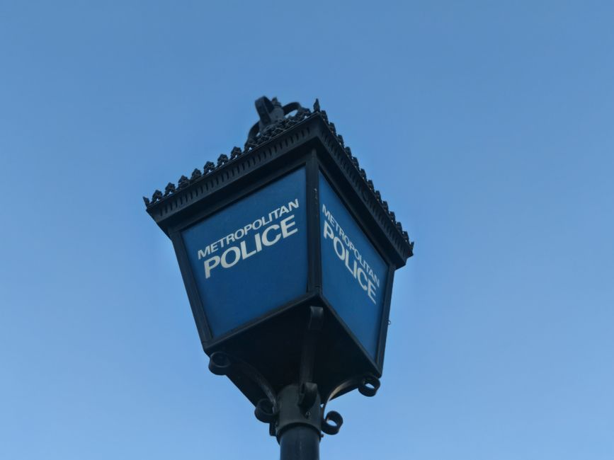 A metal street sign attached to a grey pole indicates no parking with a red circle and slash over a black 'P' symbol, and features a small black arrow pointing to the right. The background shows a day
