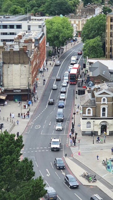 A clear view of a city street during daytime with traffic lights and lampposts along the pavement. In the background, there are historic church towers and a prominent clock tower with detailed archite
